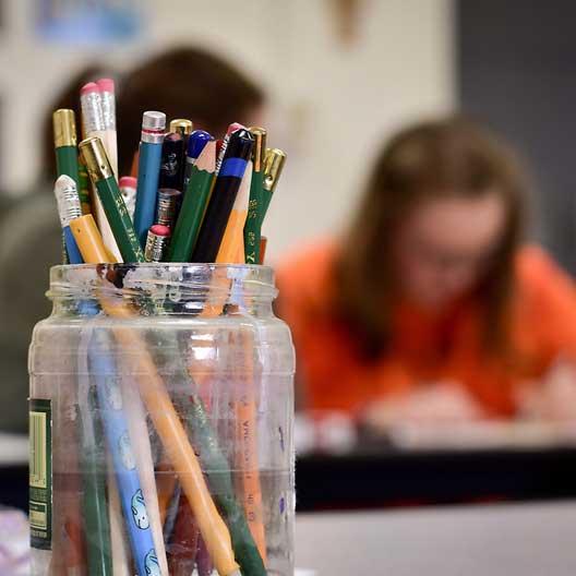 一罐铅笔，背景是一个正在工作的学生